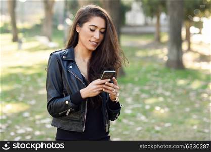 Young woman using a smartphone in an urban park. Girl wearing leather jacket.