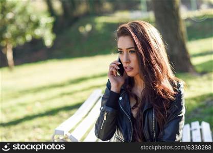 Young woman using a smartphone in an urban park. Girl wearing leather jacket.