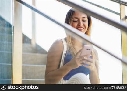 Young woman using a touchscreen smartphone wearing casual clothes. Girl sitting outdoors.. Girl using a touchscreen smartphone wearing casual clothes