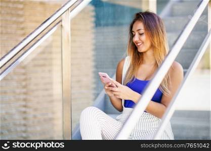 Young woman using a touchscreen smartphone wearing casual clothes. Girl sitting outdoors with gel nails.. Girl using a touchscreen smartphone wearing casual clothes