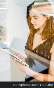 Young woman using digital tablet, photographed through glass