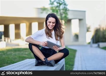 Young woman using digital tablet sitting outdoors in urban background.. Middle-age woman using digital tablet sitting outdoors in urban background.