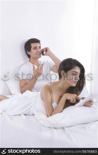 Young woman using digital tablet with man on call in bedroom
