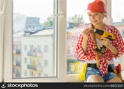 Young woman using drill to fix or installing windows. Girl working at flat remodeling. Building, repair and renovation.. Woman using drill to fix or installing windows