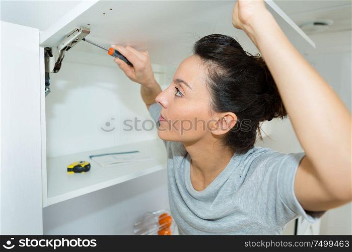 young woman using electric screwdriver to installation kitchen furniture