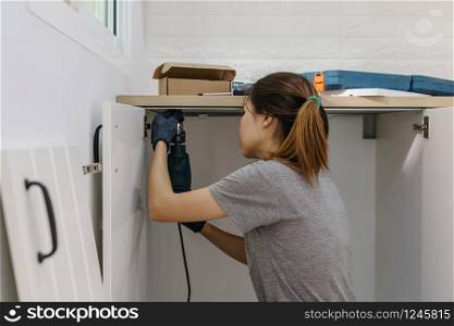 Young woman using electric screwdriver to installation kitchen furniture, DIY concept. Young woman using electric screwdriver to installation