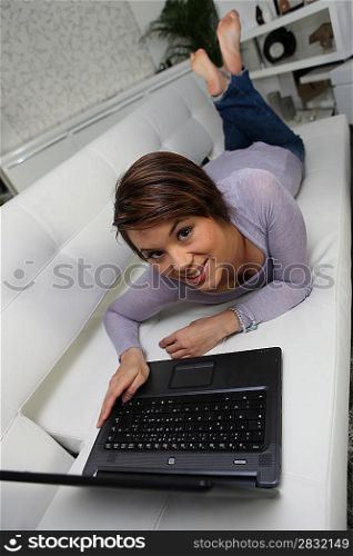 Young woman using her laptop while lying on a couch