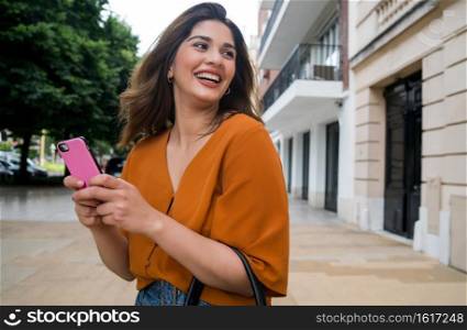 Young woman using her mobile phone while standing outdoors on the street. Urban and communication concept.