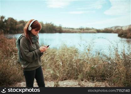 Young woman using her smartphone near a lake with headphones