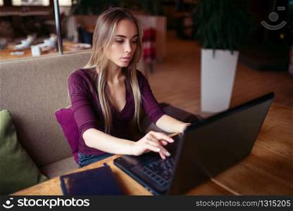 Young woman using laptop in cafe. Female with digital gadget using wifi in cafe.. Young woman using laptop in cafe.
