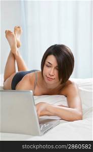 Young woman using laptop lying on bed