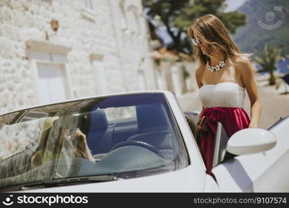 Young woman using mobile phone and standing by cabriolet car at hot summer day