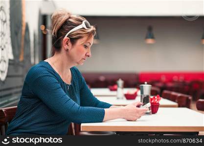Young woman using mobile phone sitting by a table in cafe