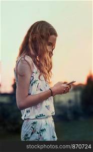 Young woman using mobile phone smartphone standing in a backyard. Candid people, real moments, authentic situations
