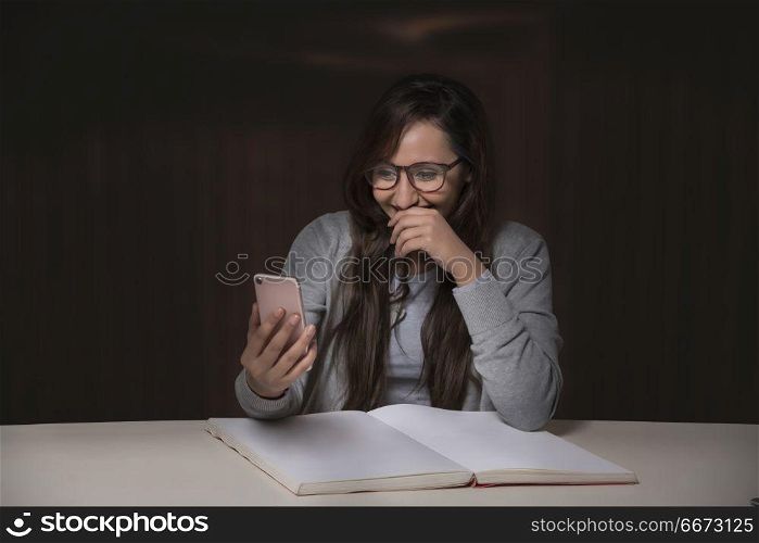 Young woman using mobile phone while reading book