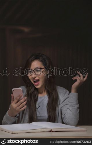 Young woman using mobile phone while reading book