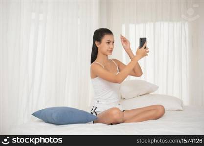 Young Woman Using Mobile Phone While Sitting On Bed At Home