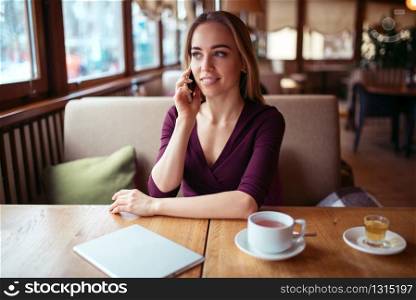 Young woman using phone in cafe. Businesswoman talking by smartphone while citting in cafe.