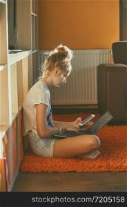 Young woman using portable computer and mobile phone, sitting on a floor, learning online at home. Candid people, real moments, authentic situations