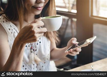 Young woman using smart phone and drinking coffee in cafe