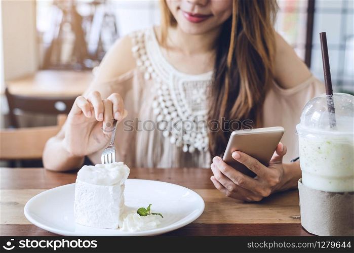 Young woman using smart phone and eating cake in cafe
