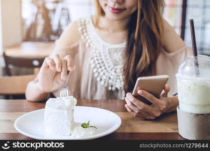 Young woman using smart phone and eating cake in cafe