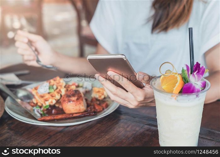 Young woman using smart phone and enjoy eating dessert in cafe on vacation trip. Young woman using smart phone and enjoy eating dessert in cafe