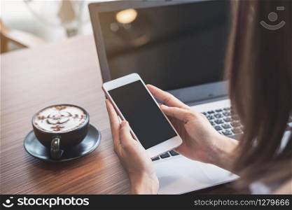 Young woman using smart phone and laptop with cup of coffee in cafe