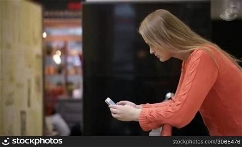 Young woman using smartphone leaning on the chair. Side view.