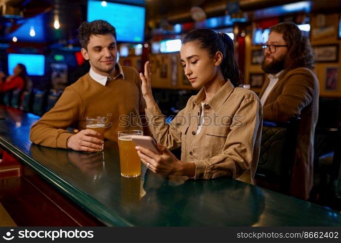 Young woman using smartphone sitting at bar counter and rejecting man. Uninterested meeting, failed flirting concept. Young woman sitting at bar counter rejecting man