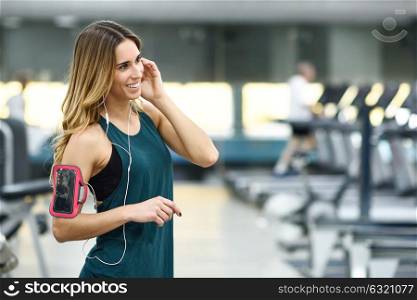 Young woman using smartphone standing in the gym before the training. Beautiful girl smiling.