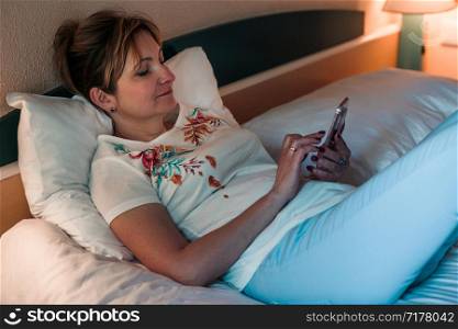 Young woman using smartphone while laying in bed in bedroom