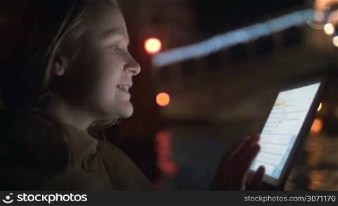 Young woman using tablet computer to chat while traveling by boat in night Venice. Communication and enjoying old city