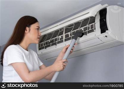 young woman using vacuum cleaner to cleaning the air conditioner at home