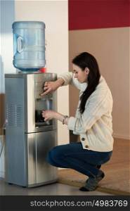 Young woman using water dispenser at office