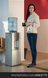 Young woman using water dispenser at office