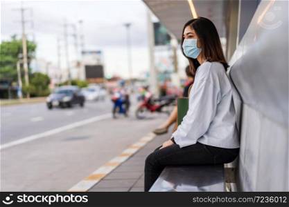 young woman waiting for bus at bus stop in city street and wearing face mask protective for spreading of coronavirus(covid-19) pandemic, new normal concept