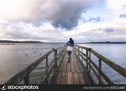 Young woman walking alone on a rustic wooden bridge over the Chiemsee lake, also called the Bavarian Sea, located near Rosenheim, Germany.