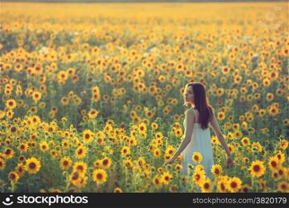 Young woman walking away in a field of sunflowers, view from her back; copy space