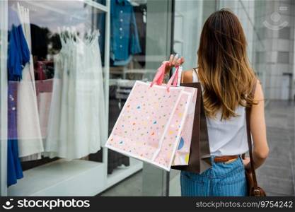 Young woman walking in front of clothing store with shopping bags, surrounded by busy urban buildings and bustling transportation. She is a trendy shopper, always following the latest fashion trends.