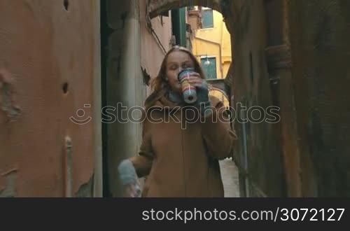 Young woman walking in the street in Venice, Italy. She having a phone talk and drinking coffee during the way