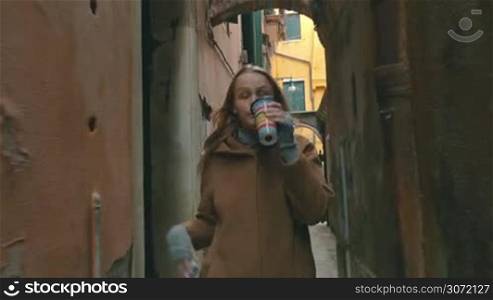 Young woman walking in the street in Venice, Italy. She having a phone talk and drinking coffee during the way