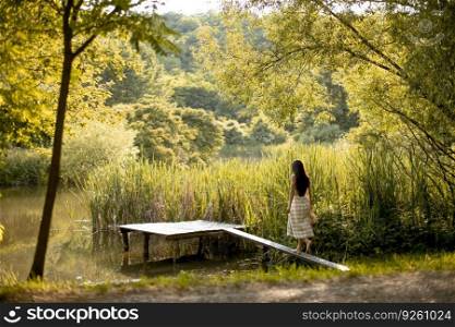 Young woman walking on the wooden pier at the calm lake on a hot summer day