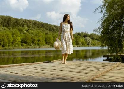 Young woman walking on the wooden pier at the calm lake on a hot summer day