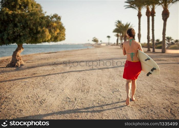Young woman walking through the beach with her surfboard