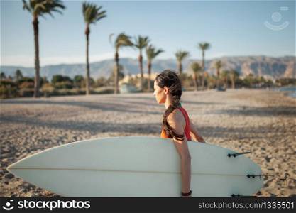 Young woman walking through the beach with her surfboard