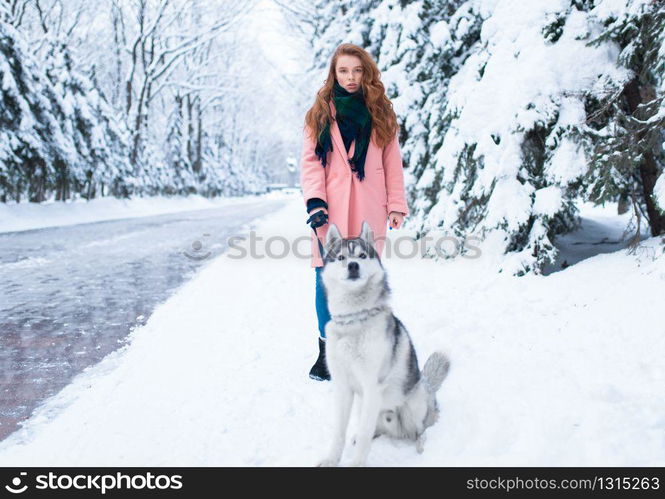 Young woman walks in the park with siberian husky, snowy forest on background. Cute girl with charming dog. Young woman walks in the park with siberian husky