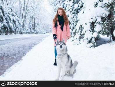 Young woman walks in the park with siberian husky, snowy forest on background. Cute girl with charming dog. Young woman walks in the park with siberian husky