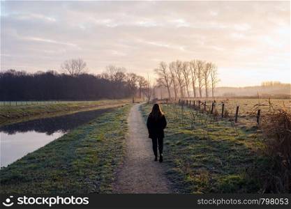 Young woman walks on a cold day by the river in the sunset, beautiful landscape background colorful nature. Young woman walks on a cold day by the river in the sunset, beautiful landscape background colorful