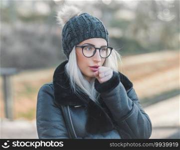 Young woman warming her hands, wearing warm clothing, november day outdoors. Cute girl feeling cold. Winter concept. Female person in cold weather.